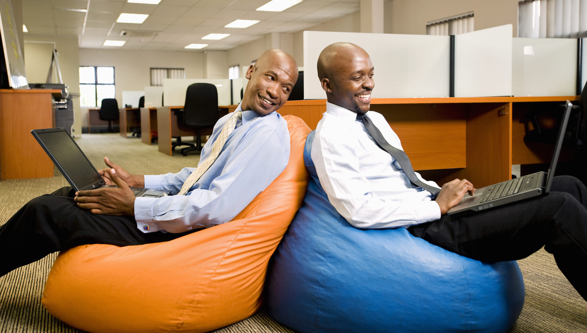 Two businessmen compare work on laptops while sitting on beanbags. Pretoria, South Africa