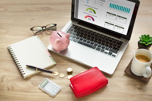 Piggy bank, laptop, purse with money, coffee cup on wooden table top.