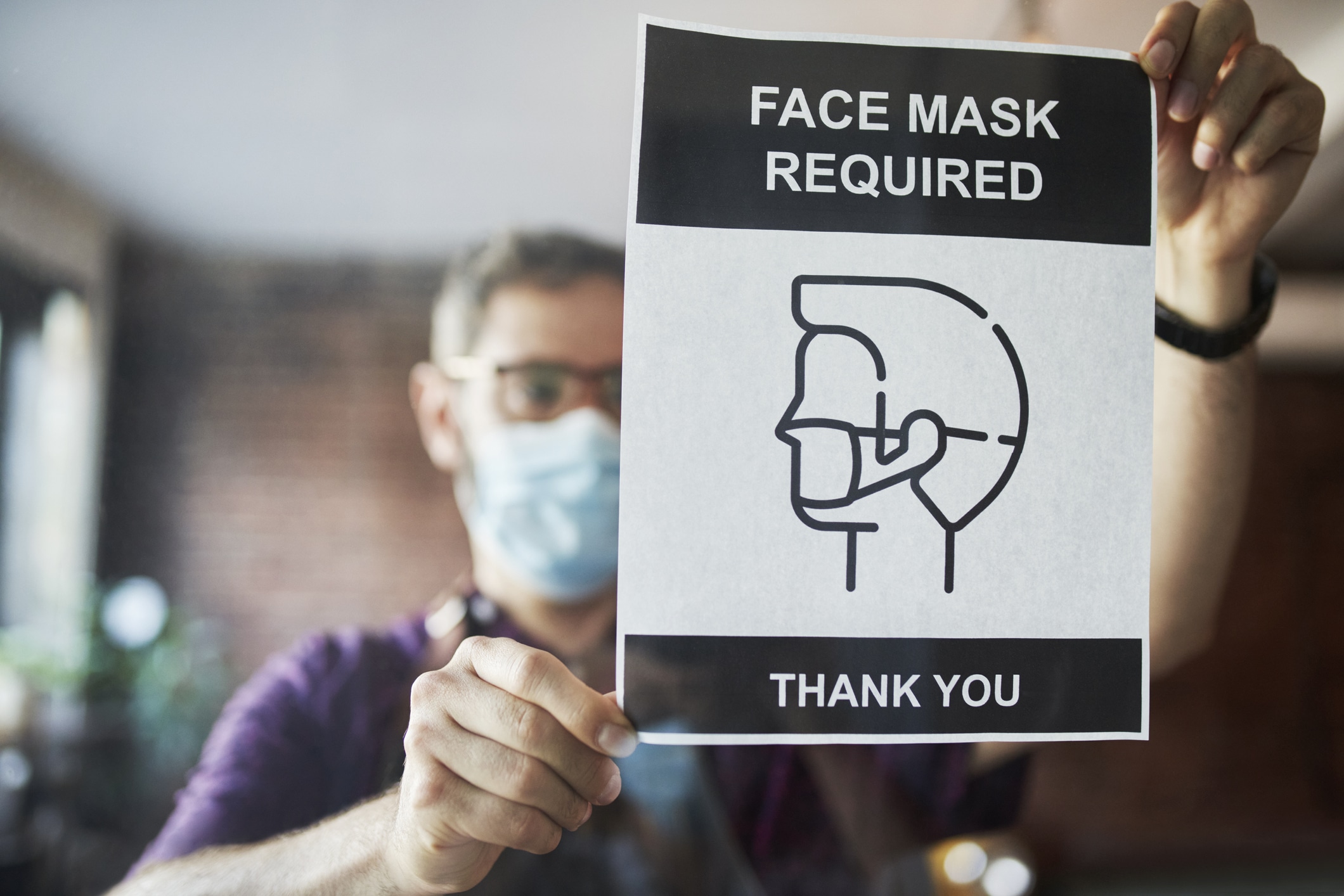 Business owner setting up face mask required sign in cafe window