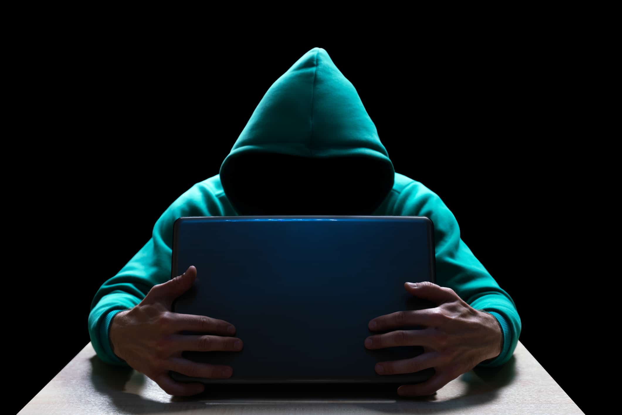 Unknown person in the hood, reaches out from the darkness to the laptop. Theft of household and computer equipment