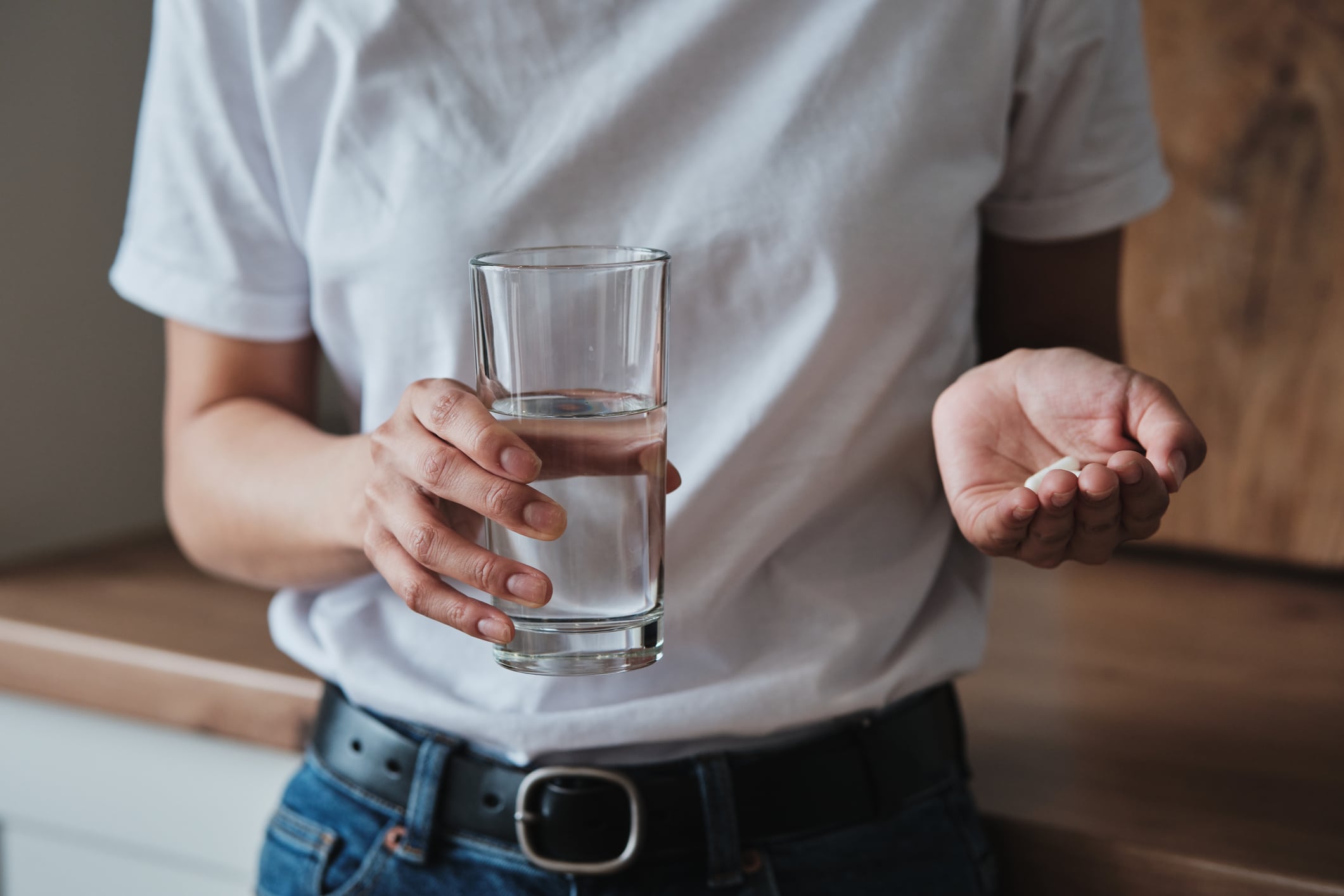 Woman holding pills and glass of water while standing in kitchen at home