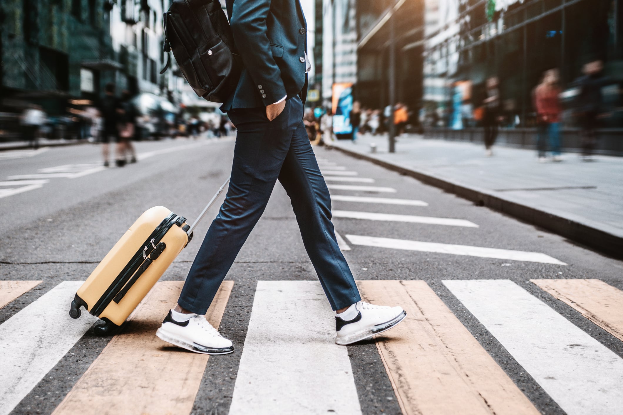 Business travel concept. Man walking on city street with yellow suitcase cabin bag